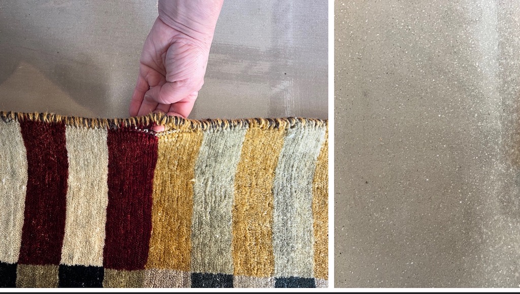 Close-up of a hand inspecting worn rug binding on a handmade striped wool rug, showing frayed edges before repair at Rug Master in San Francisco, CA — specialists in hand and machine rug binding.