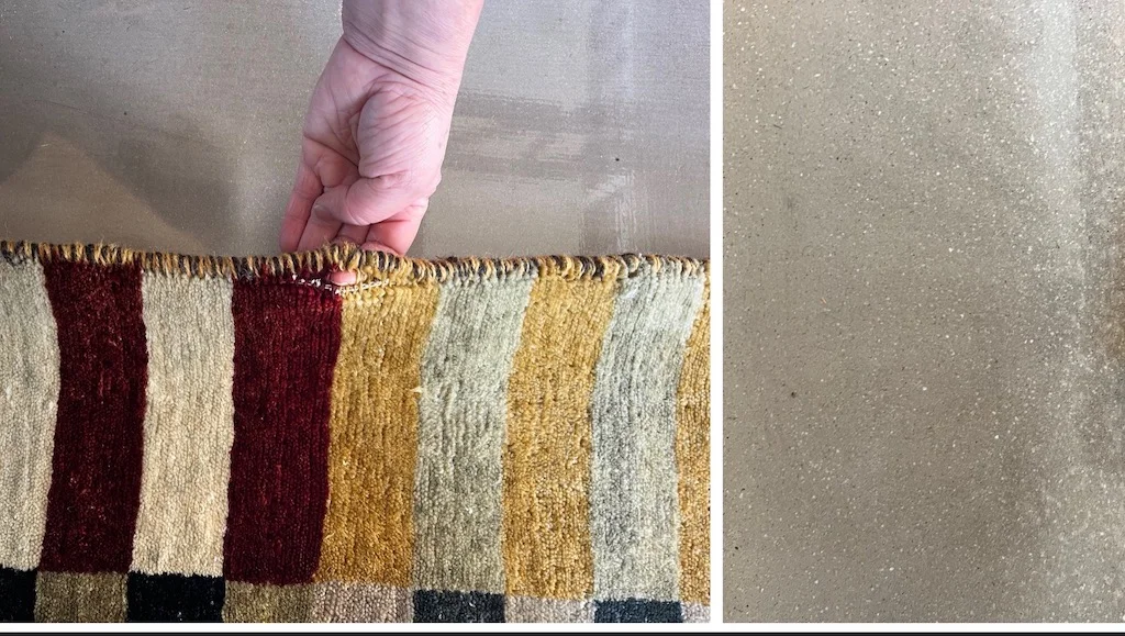 Close-up of a hand inspecting worn rug binding on a handmade striped wool rug, showing frayed edges before repair at Rug Master in San Francisco, CA — specialists in hand and machine rug binding.